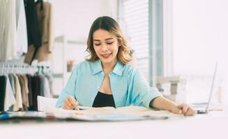 asiático mujer diseñador ocupado haciendo ropa trabajo o estudiar en Moda diseño estudio foto