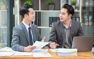 Asian business team consists of marketing staff. accountant and financial officer Help each other analyze company profits using tablets. calculator Laptop computers, graph paper, and corporate pens. photo