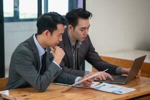 Asian business team consists of marketing staff. accountant and financial officer Help each other analyze company profits using tablets. calculator Laptop computers, graph paper, and corporate pens. photo