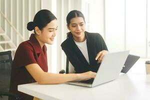 Young adult woman wearing black suit teach lady intern using laptop brief for work in office photo