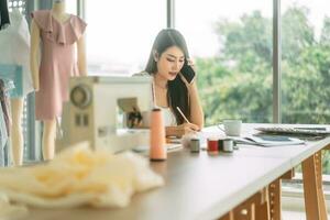Young adult asian woman designer using phone busy work in workshop photo
