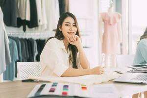 asiático mujer diseñador ocupado haciendo ropa trabajo o estudiar en Moda diseño estudio foto