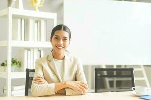 Portrait of young adult southeast business woman with smile teeth confident wearing white suit sitting in office photo