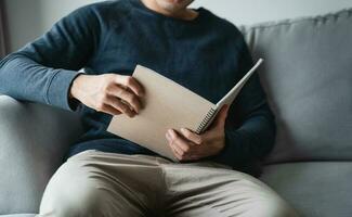 Man reading the notebook sitting on the sofa at home. photo