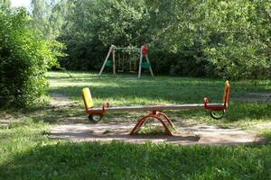 Swings on the playground. In the background are trees. Summer in the city photo