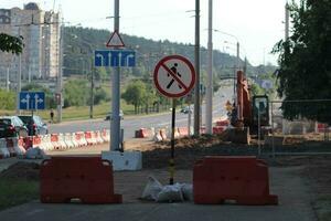 Construction work in the city in summer. Wide road repair. Warning road sign, barriers and excavator photo