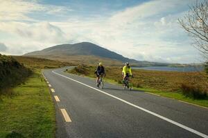 Galway, Ireland, 2023, group of cyclists cycling trough connemara by the lough inagh with mountains in the background, county Galway, Ireland photo