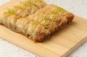 Pieces of baked baklava in honey and sprinkled with pistachios on a wooden board photo