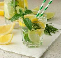 Lemonade in a transparent glass with lemon, lime, rosemary sprigs and mint leaves on a white background photo