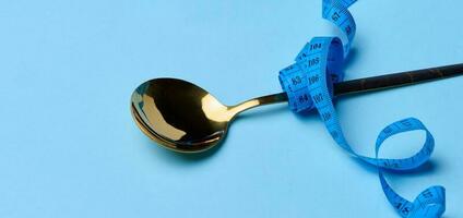 Empty spoon wrapped with centimeter on blue background, weight loss concept photo