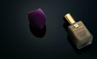 CHONBURI, THAILAND-DECEMBER 15, 2022 Jovina makeup sponge and Estee Lauder makeup foundation bottle on dark background. Liquid beige make-up foundation and beauty blender on black background. photo