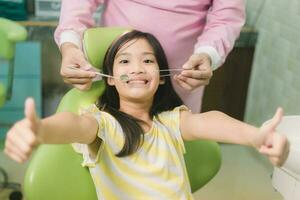 Portrait of happy asian girl shows thumb up gesture at dental clinic photo