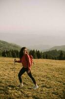 Young woman is taking a scenic hike on a hill, carrying all her necessary gear in a backpack photo