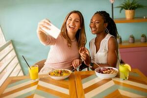 Two young women, caucasian and black one, taking selfie with mobile phone in the cafe photo