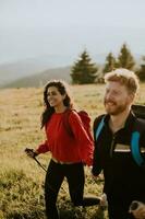 Young couple walking with backpack over green hills photo