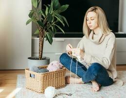 Young woman knitting warm scarf indoors photo