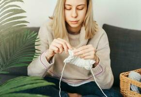 Young woman knitting warm scarf indoors photo