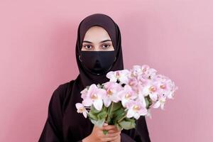 recortado imagen de árabe joven niña en hiyab, protector máscara y participación orquídea ramo. generativo ai. foto