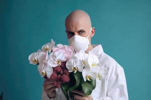 Closeup Portrait of Bald Man in Protective Mask and Holding Flower Bouquet on Pastel Teal Background. . photo