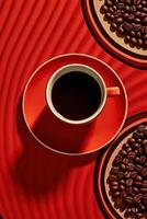 A Cup of Coffee with Saucer, Brown Roasted Seeds Strewn on Red Background. . photo