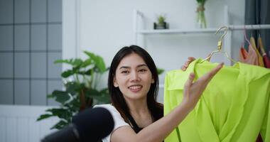 Footage of Young Asian woman and friend blogger showing clothes in front of smartphone camera while live streaming at home studio, small Business online influencer Fashion on social media concept. video