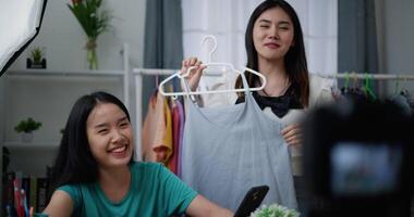 métrage lent mouvement coup de Jeune magnifique asiatique femmes vivre diffusion à vente mode vêtements à Accueil studio, elles ou ils sont parlant dans de face de numérique caméra, influenceur sur social médias concept video