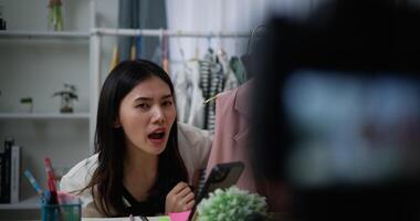 Footage of Young Beautiful Asian women live streaming at clothes shop, They are talking in front of camera and check comment on smartphone, small business online influencer on social media concept video
