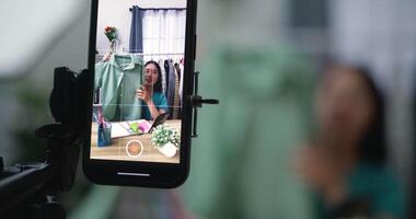 metraggio di pmi attività commerciale asiatico bellissimo donna uso mobile Telefono vivere streaming a casa studio, donne revisione Abiti Prodotto nel sfondo, piccolo attività commerciale in linea influencer su sociale media concetto. video