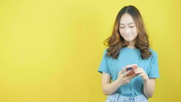 Video of Asian woman smiling while pointing left and thumbs up introducing product standing on yellow background.