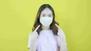 ung asiatisk kvinna rekommenderas till ha på sig en mask i offentlig på en gul bakgrund. video
