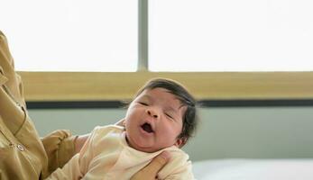 Newborn baby girl yawns in mother's arms photo