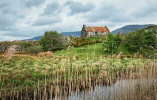 hermosa paisaje paisaje con antiguo oxidado estaño techo cabaña por el río con montañas en el antecedentes a Connemara nacional parque en condado galway, Irlanda foto