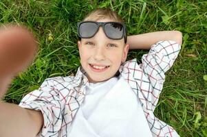 linda chico mentiras en el césped con Gafas de sol y toma un selfie foto