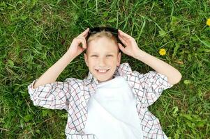 A cute boy lies in the grass and smiles, holds sunglasses on his head photo