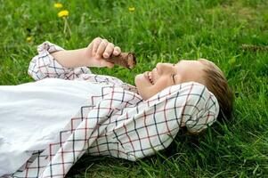 Happy boy lies on the grass and eats chocolate ice cream photo