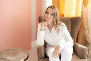 A cute girl is sitting in a chair, her hand under her face. A room with pink walls photo