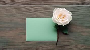 Top View of Sea Green Blank Paper Card with Beautiful Rose Flower Mockup on Wooden Table, . photo