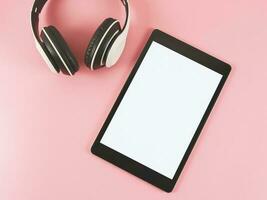 flat lay of tablet with white blank screen and headphones on pink background. photo