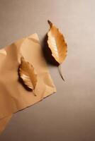 Top View of Golden Leaves and Blank Kraft Paper Mockup on Beige Background, . photo