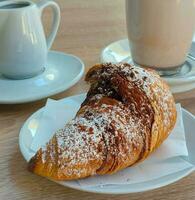Selective focus of delicious croissant poured with chocolate and sprinkled it with powder staying on plate in cafe. photo