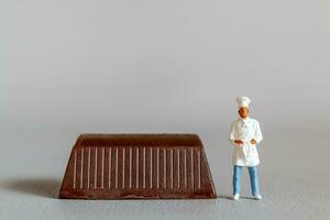 Miniature people chef with chocolate standing while standing against a gray background photo