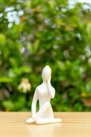 cerámico yoga figurilla de mujer haciendo yoga actitud en de madera piso y verde hoja antecedentes foto