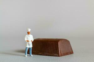 Miniature people chef with chocolate standing while standing against a gray background photo