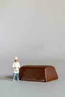 Miniature people chef with chocolate standing while standing against a gray background photo