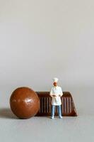 Miniature people chef with chocolate standing while standing against a gray background photo