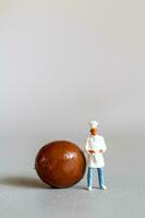 Miniature people chef with chocolate standing while standing against a gray background photo