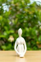 Ceramic Yoga Figurine of Woman doing yoga pose on wooden floor and green leaf  background photo