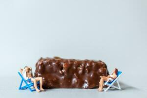 Miniature people wearing swimsuit relaxing on chocolate bars on gray background. World Chocolate Day Concept photo