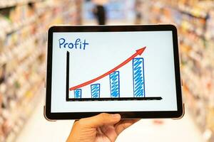 Using tablet to see business growth predication graph with blur background of department store. Business successful concept. Concept of growth planning and strategy. photo