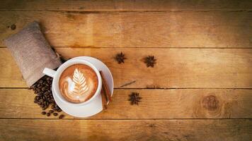 Coffee cup top view on old wooden table. Leaf pattern on cafe latte. Anise stars, coffee beans in bag and cinnamon for decoration. Beautiful, organic, natural view with best drink in the world. photo